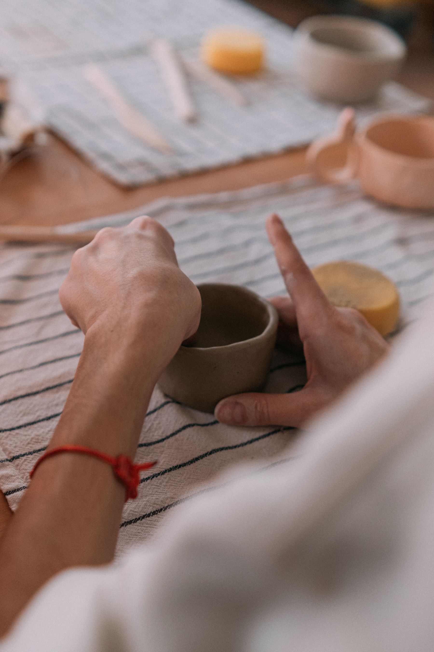 Illustrative photograph: Hands carefully shaping a clay vessel on a striped cloth in a pottery studio.