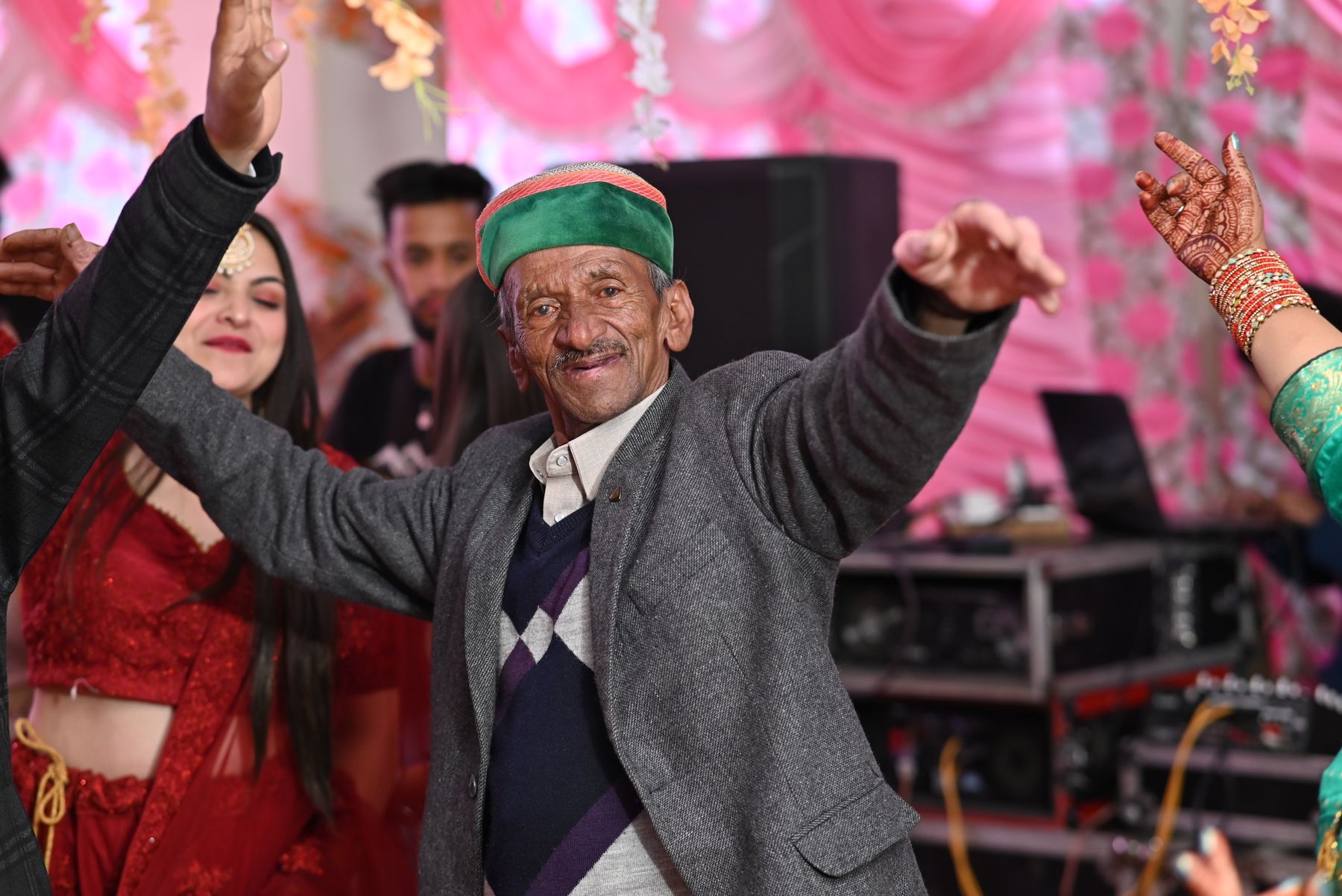 Illustrative photograph: An older man in a suit dancing with raised arms at a colourful celebration.