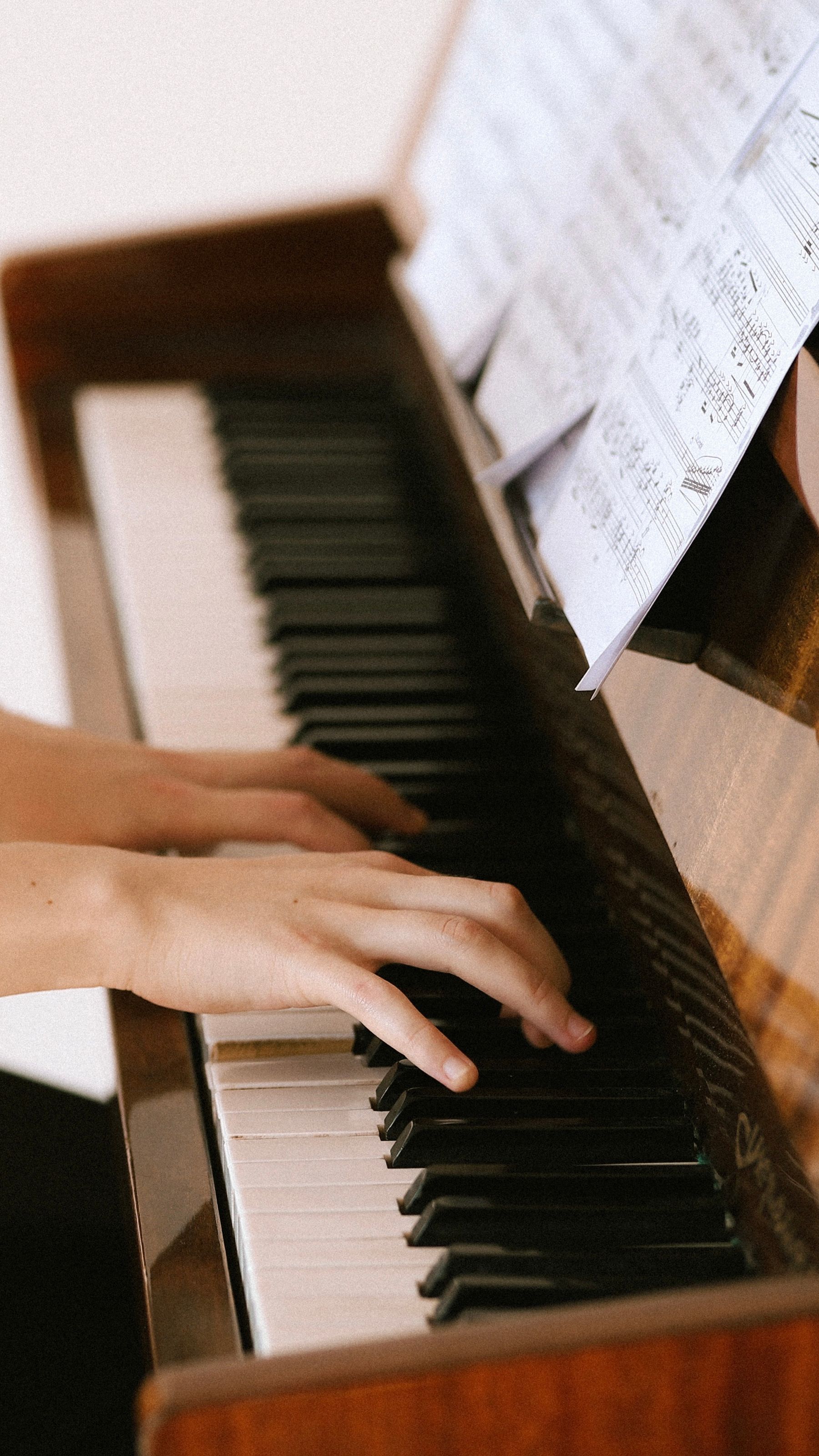 Illustrative photograph: Hands playing a piano with sheet music open above its keyboard.