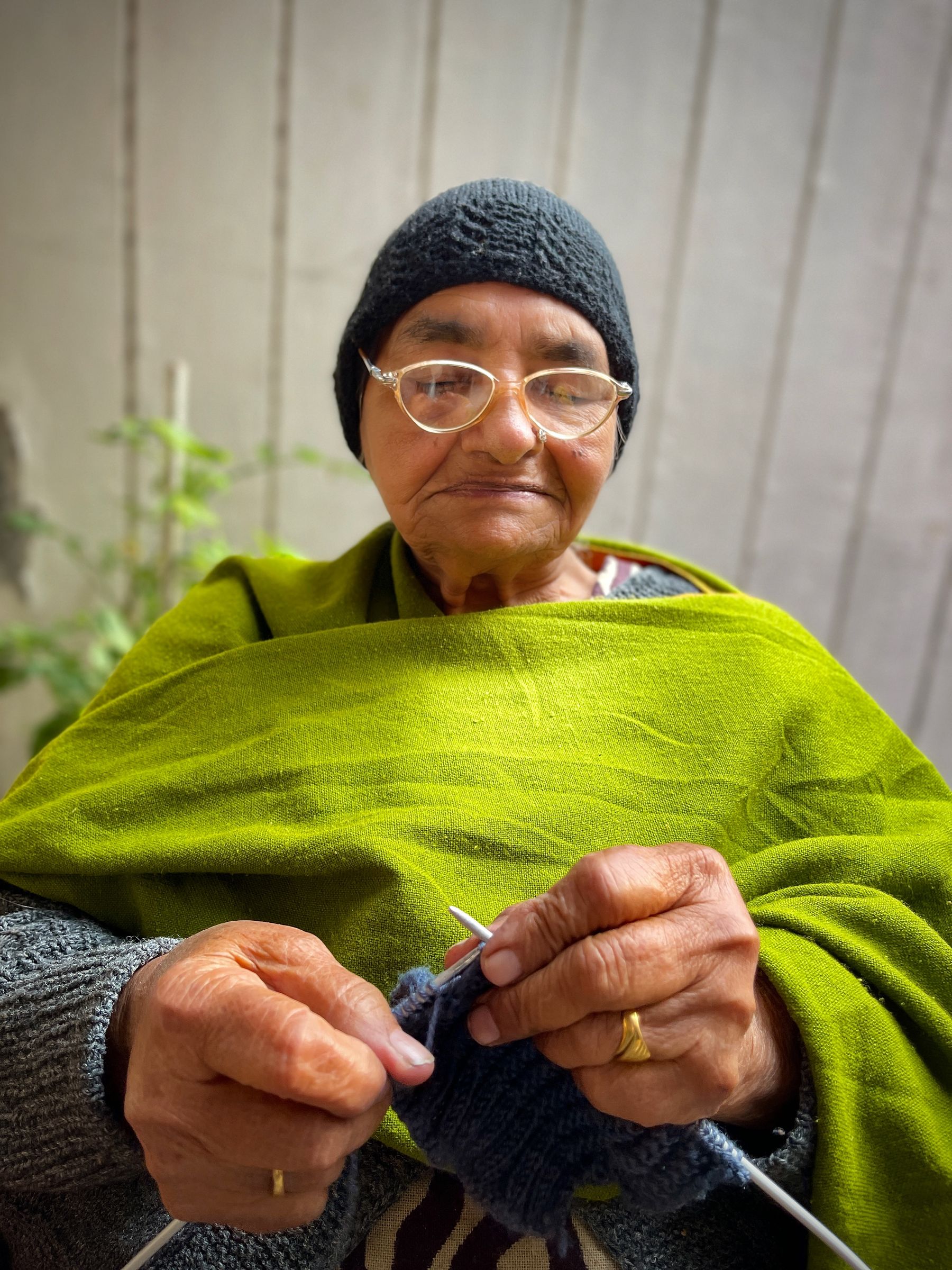 Illustrative photograph: An older woman in glasses and a bright green shawl enjoying her knitting outdoors.