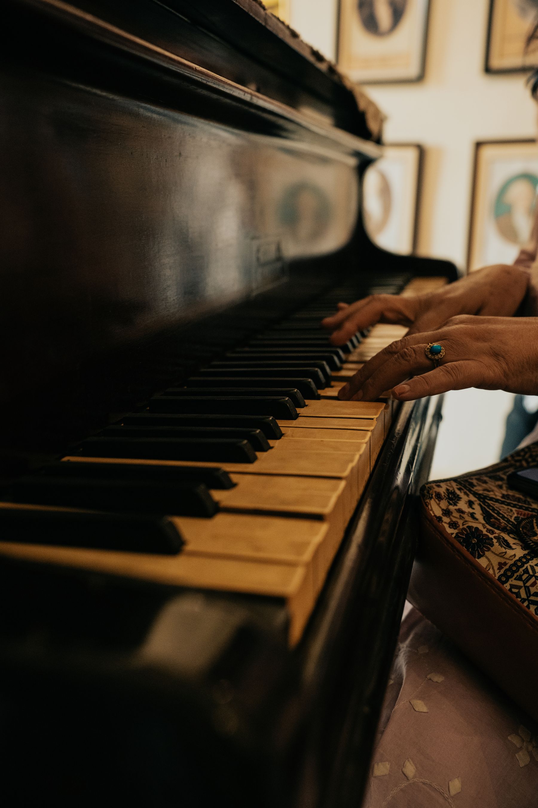 Illustrative photograph: Hands playing an antique wooden piano in a warm room with framed photographs.