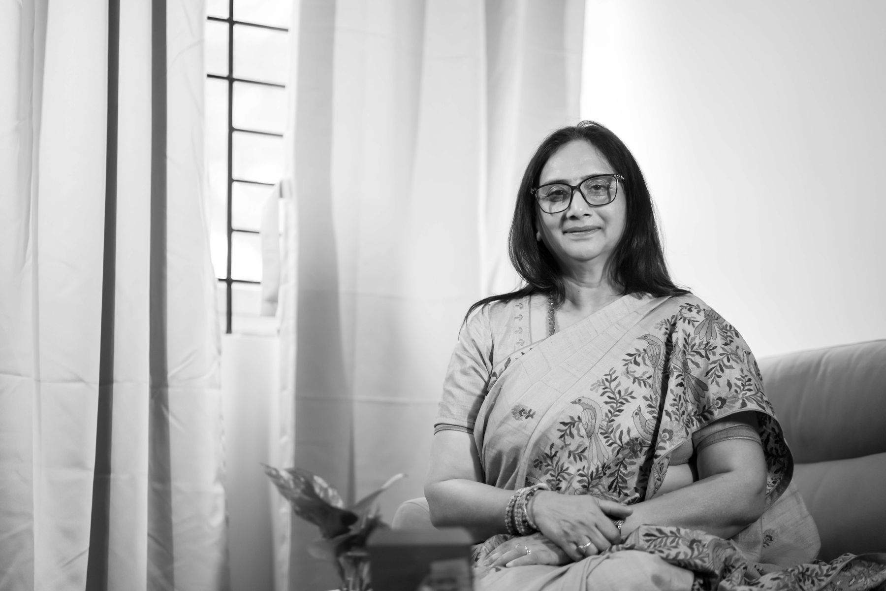 Illustrative photograph: A woman in an elegant sari seated beside a bright window, photographed in black and white.