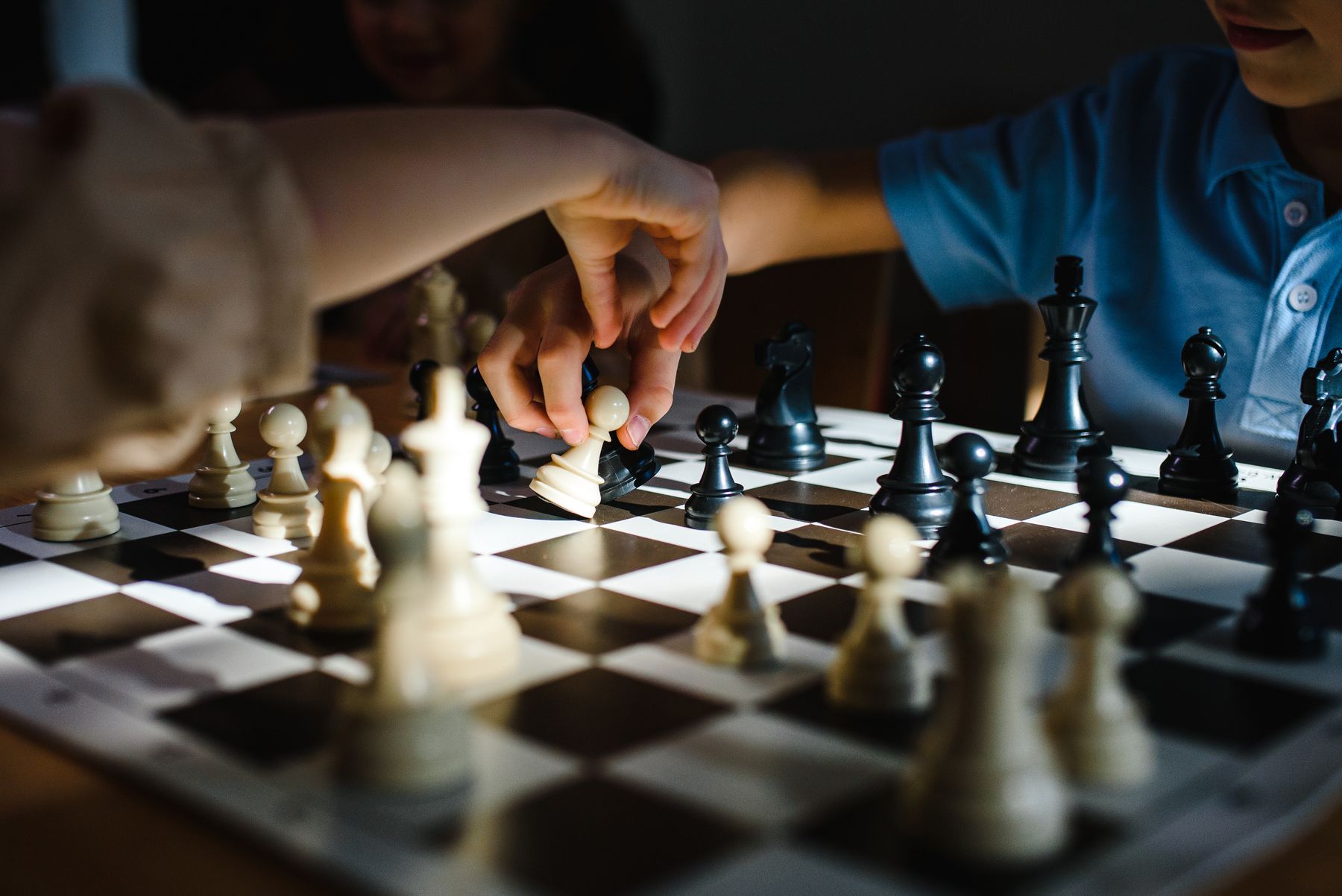 Illustrative photograph: Hands moving pieces across a chessboard in warm indoor light.